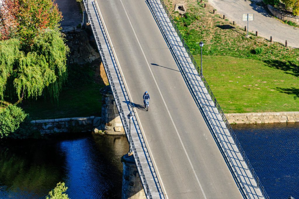 Ilmakuva pyöräilijästä sillalla kesäisessä järvimaisemassa.